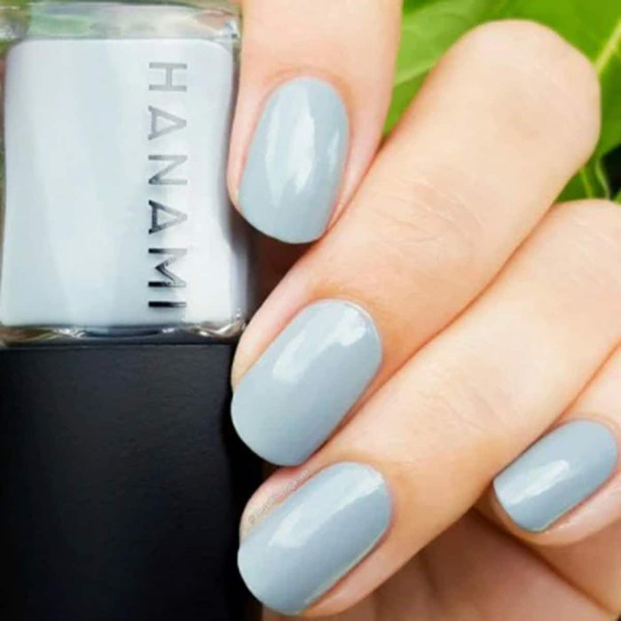 Hand with light blue nails holding a bottle of Hanami nail polish.