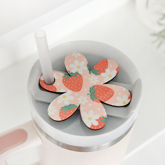 Pink tumbler with straw, topped with a Coconut Lane flower-shaped topper decorated with strawberries and floral designs.
