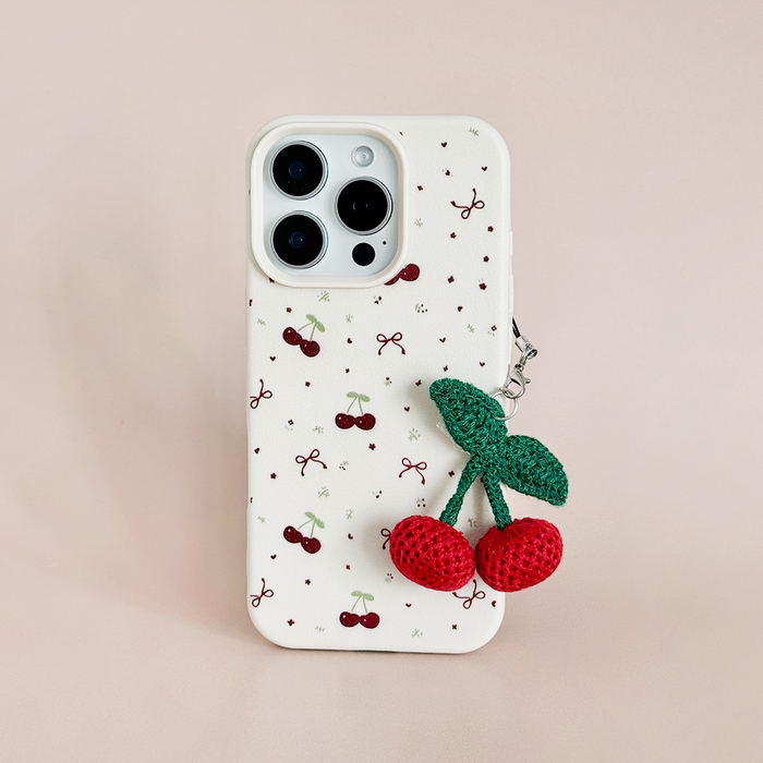 White phone case with cherry print and a cherry-themed Coconut Lane phone charm on a light pink background.