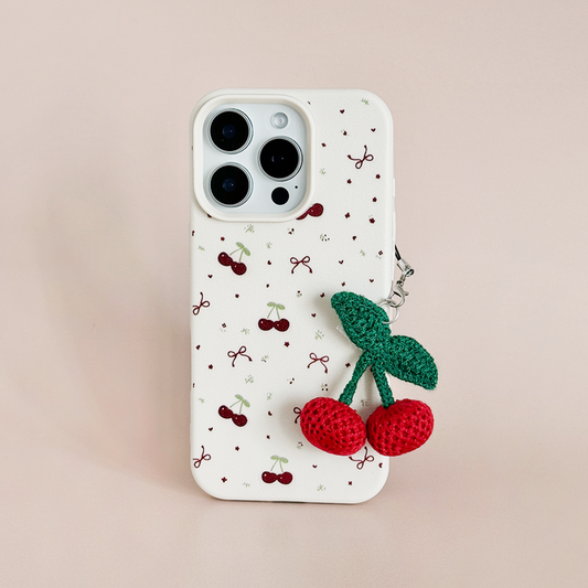 White phone case with cherry print and a cherry-themed Coconut Lane phone charm on a light pink background.