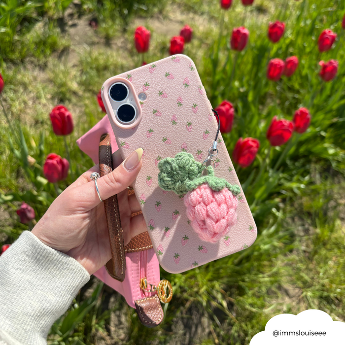 Pink phone with Coconut Lane pink strawberry phone charm held among red tulips in bright sunlight.