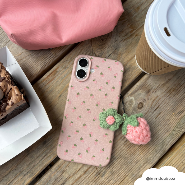 Pink phone with a Coconut Lane pink strawberry charm and matching case on a table beside coffee, cake, and a pink bag.