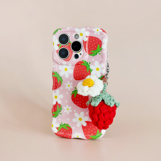 Pink phone case with strawberry and daisy print, red beaded strawberry charm, and crocheted flower charm attached.