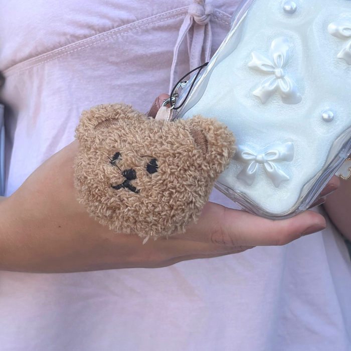 Coconut Lane Teddy phone charm with white bows, held by someone wearing a pale pink top.