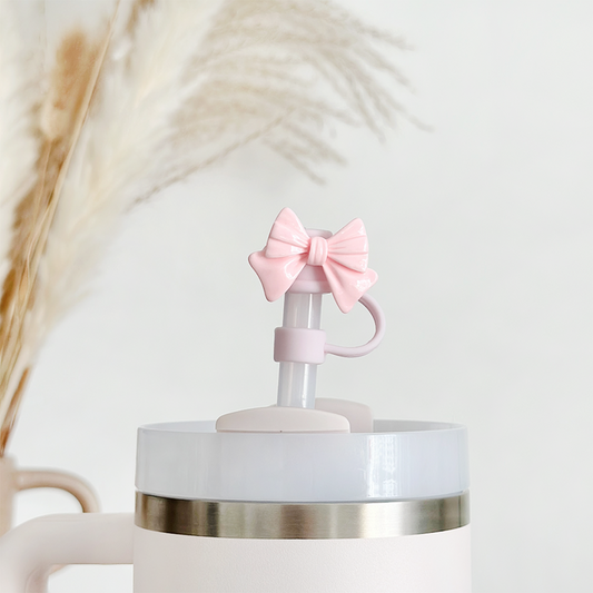 Pale tumbler with a pink bow straw cover, placed in front of beige pampas grass.
