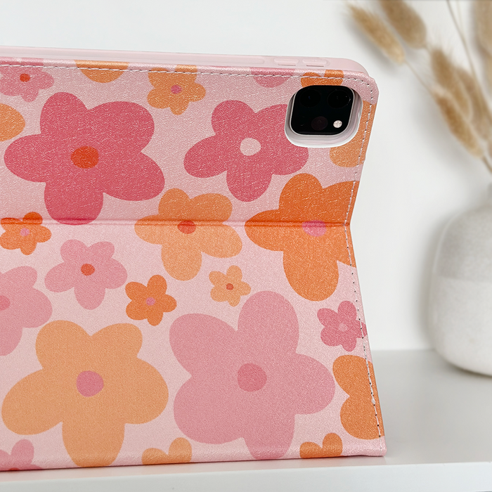 Pink and orange floral iPad case on a tablet next to a white vase with dried grass in a bright room.