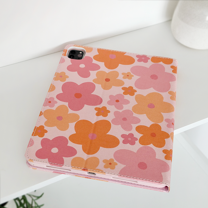 Tablet in a pink and orange floral iPad case on a white shelf next to a plant and white vase.