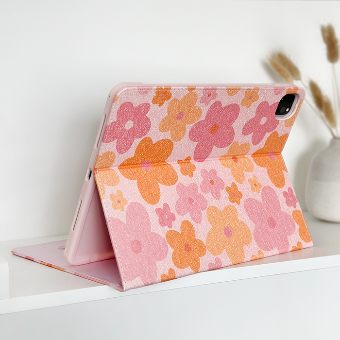 Pink and orange floral iPad case on a white shelf next to a small white vase holding dried grass.