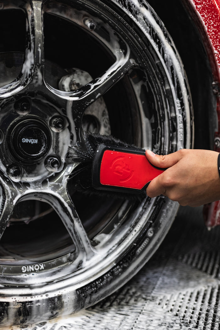 A person using a Detail Factory Wheel Face Brush Red to clean a red vehicle's tire.
