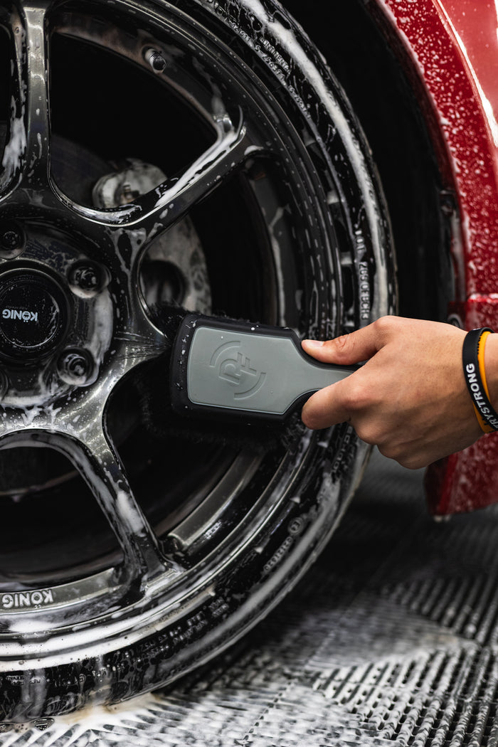 A person using a Detail Factory Wheel Face Brush Grey to clean a red vehicle's tire.