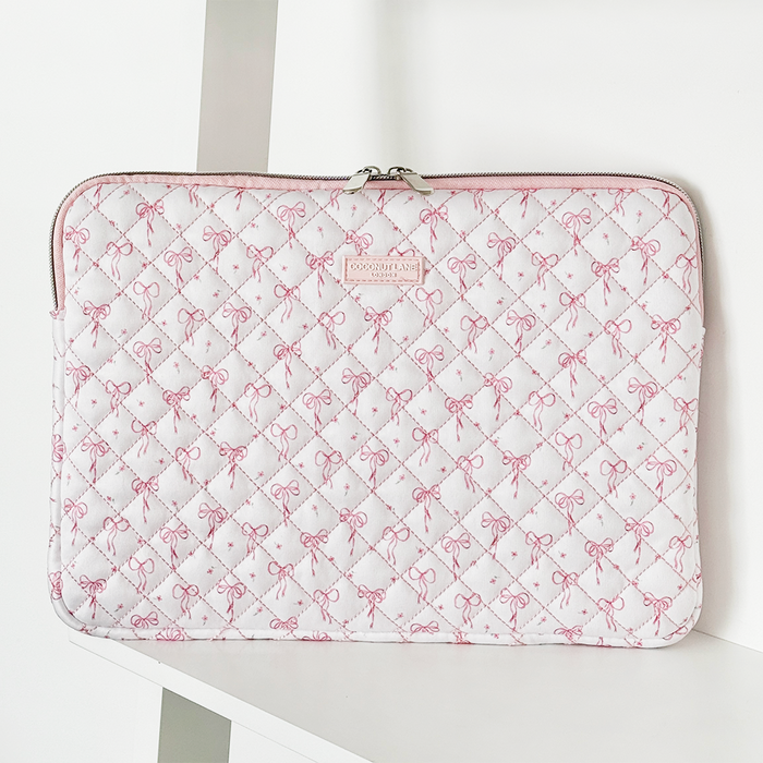 Quilted laptop sleeve with dainty bow pattern and zipper, displayed on a white shelf.