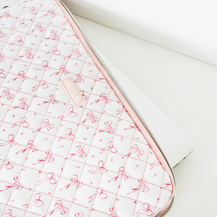 White laptop partially inside a pink quilted Coconut Lane Dainty Bows laptop sleeve on a white surface.