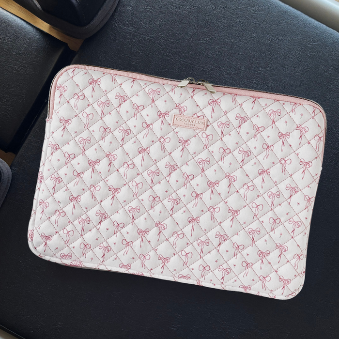 Quilted laptop sleeve with dainty bow pattern and pink accents on a dark cushion.