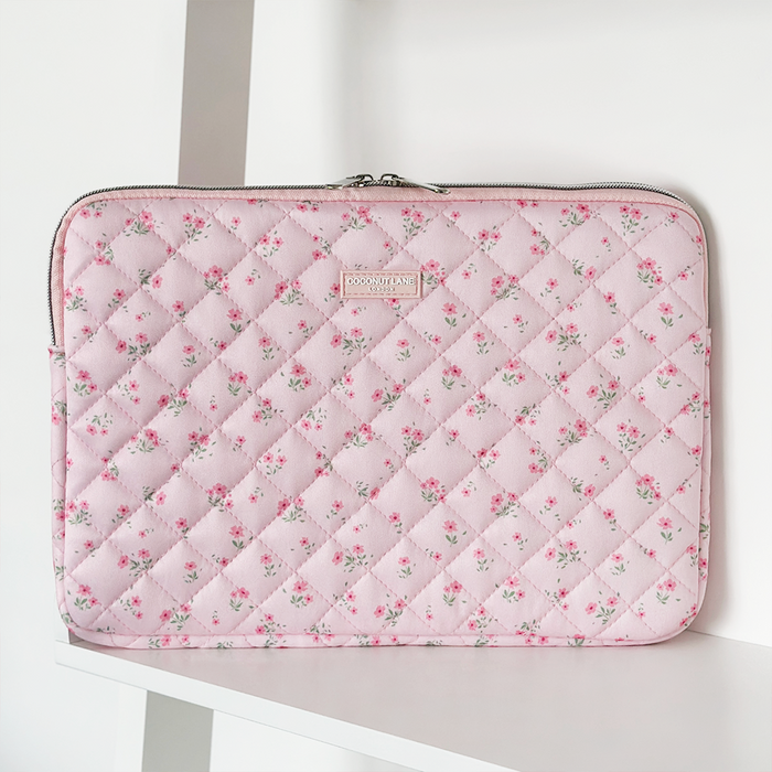 Pink quilted laptop sleeve with ditsy floral pattern, standing upright on a white shelf.