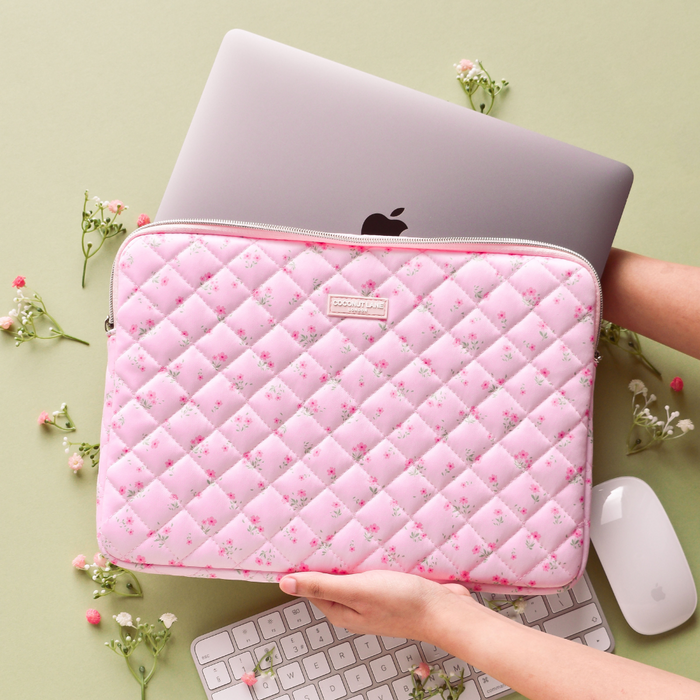 Pink quilted floral Coconut Lane laptop sleeve held with a silver laptop on a green surface.