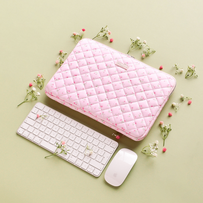 Pink quilted floral laptop sleeve beside a white keyboard and mouse on a green background.