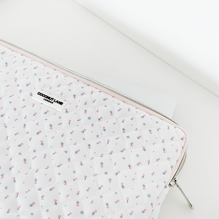 White quilted laptop sleeve with ditsy floral pattern, partially unzipped to show a silver laptop inside.