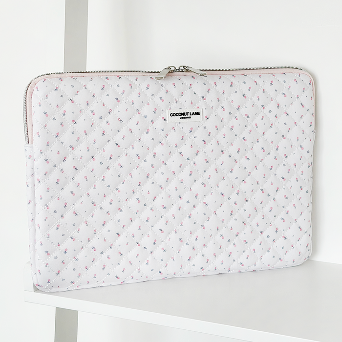 White quilted laptop sleeve with ditsy floral pattern on a white shelf.