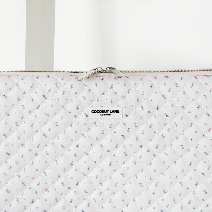 White quilted laptop sleeve with small floral print and zipper closure.