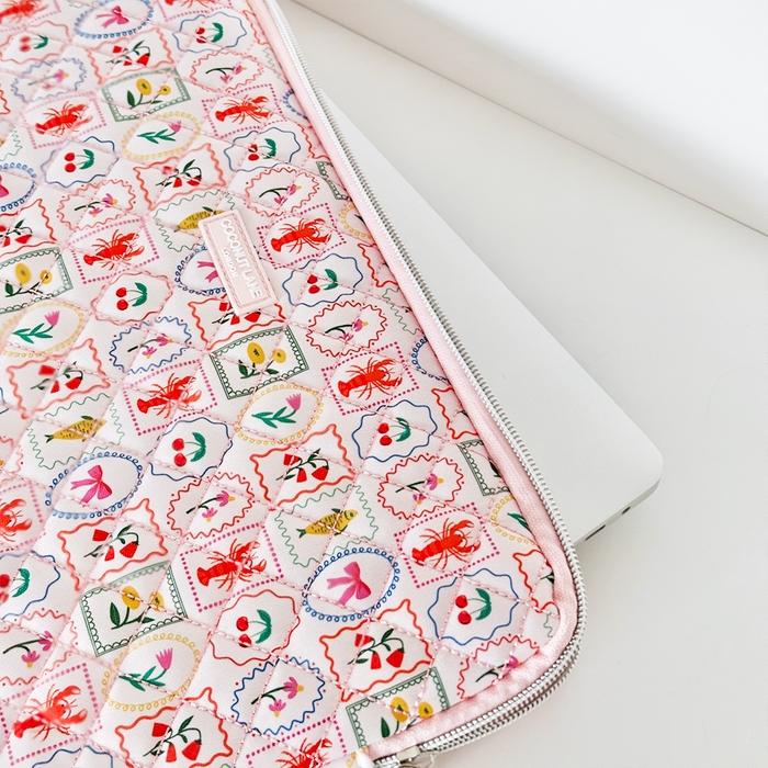 Quilted pink Dolce Vita laptop sleeve with zipper partially covering a silver laptop on a white surface.