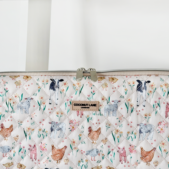 Quilted laptop sleeve by Coconut Lane with playful cows, sheep, and chickens on a farmyard pattern.