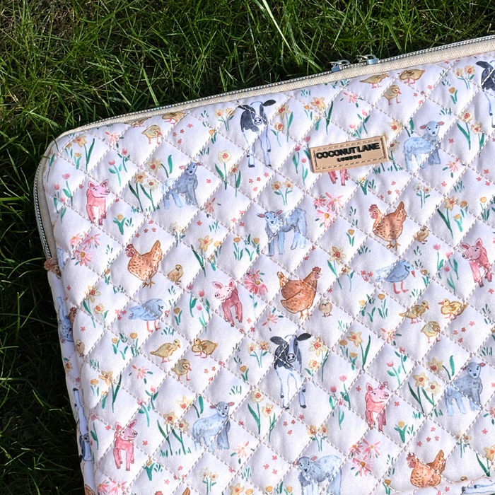 Quilted laptop sleeve with colorful farmyard patterns by Coconut Lane, displayed on green grass.