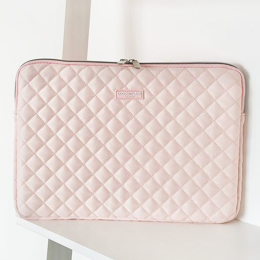 Pink quilted Coconut Lane laptop sleeve with zipper, standing upright on a white shelf.
