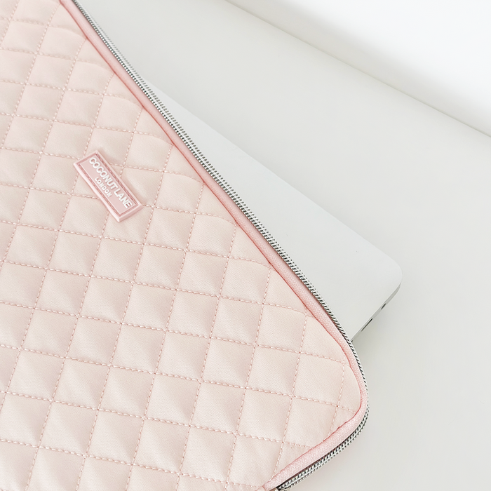 Silver laptop partially in a pink quilted Coconut Lane laptop sleeve on a white surface.