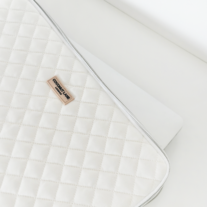 Quilted white Coconut Lane laptop sleeve with zipper, partially covering a silver laptop.