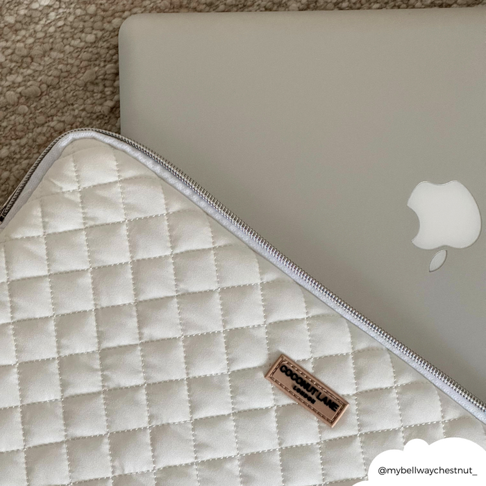 Quilted cream laptop sleeve with a silver MacBook, shown on a textured beige background.