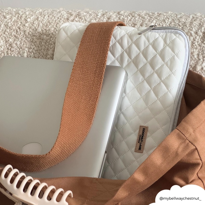 Silver laptop with coconut-patterned quilted sleeve in a brown bag on a textured surface.