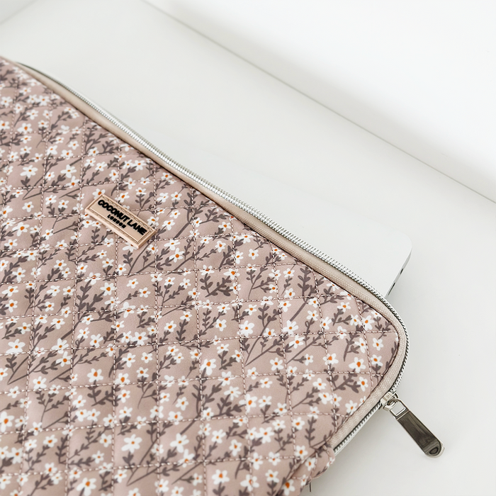 Laptop halfway inside coconut lane quilted laptop sleeve with nude floral pattern and zipper on a white surface.