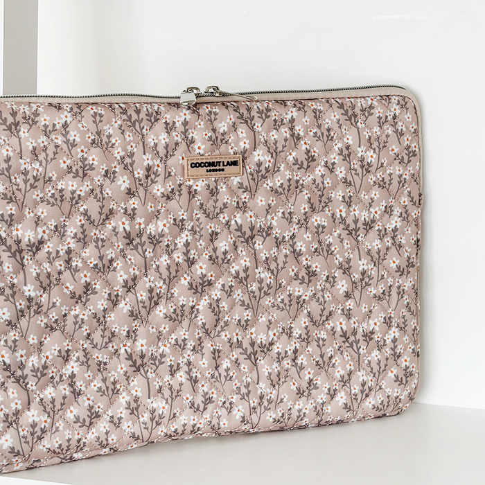 Quilted laptop sleeve with nude floral pattern, padded finish, and zipper closure.