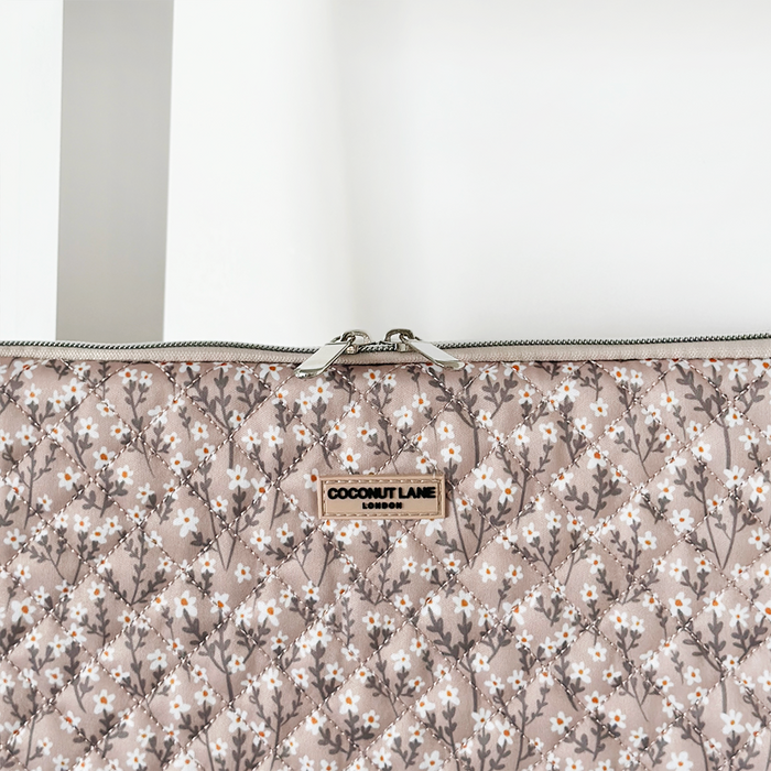 Nude quilted laptop sleeve with floral pattern, visible zipper, and a small front label.