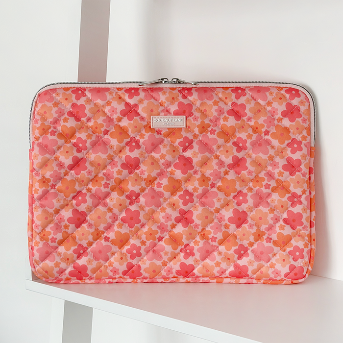 Quilted pink and orange Coconut Lane laptop sleeve on a white shelf with plain background.