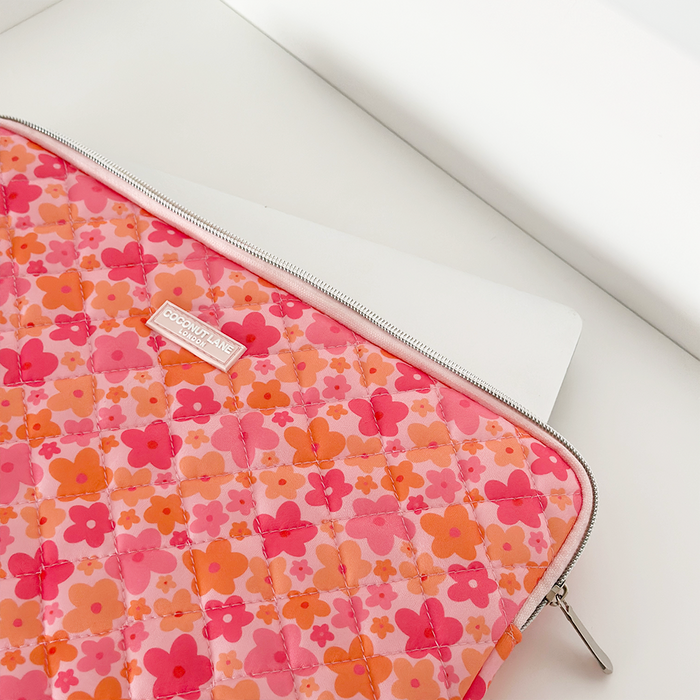 White laptop partially tucked in a quilted pink and orange floral Coconut Lane laptop sleeve on a white surface.