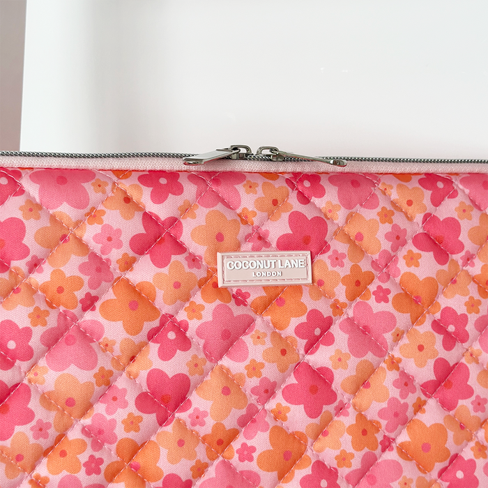 Quilted laptop sleeve in pink and orange floral pattern with zipper and front Coconut Lane logo label.