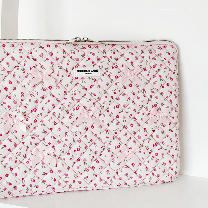 Quilted pink laptop sleeve with watercolor flower pattern and bow accents, displayed on a white shelf.