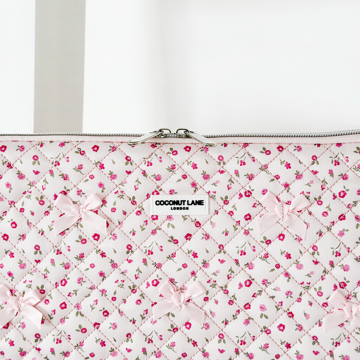 Quilted laptop sleeve with pink watercolor flower pattern, pink bows, Coconut Lane label, partially unzipped.