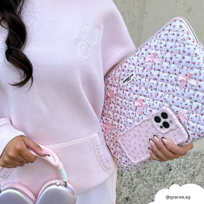 Woman in a light pink hoodie holds pink headphones and a quilted laptop sleeve with pink watercolor flower pattern.
