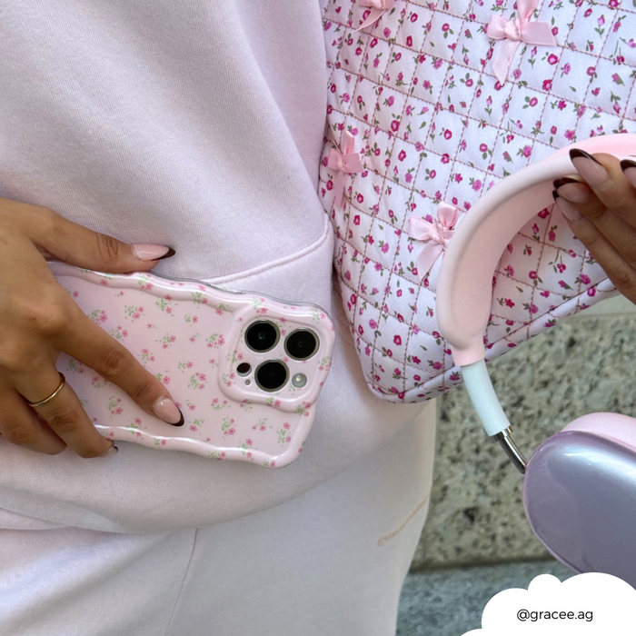 Woman in a pink outfit holding a floral phone case, quilted bag, pink headphones, and pink floral laptop sleeve.
