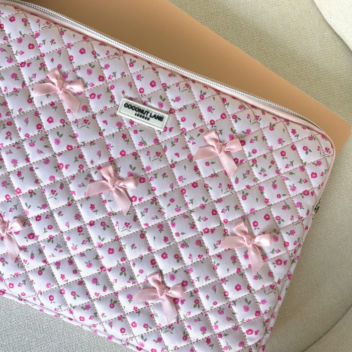 Quilted pink laptop sleeve with watercolor flower pattern, partially unzipped to show a gold laptop inside.