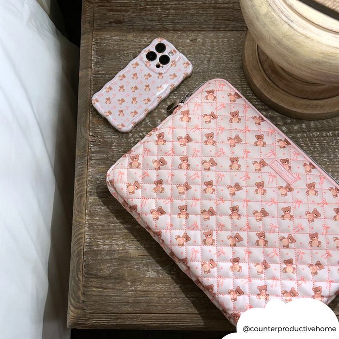 Quilted beige Coconut Lane laptop sleeve and matching teddy phone case on a wooden nightstand.