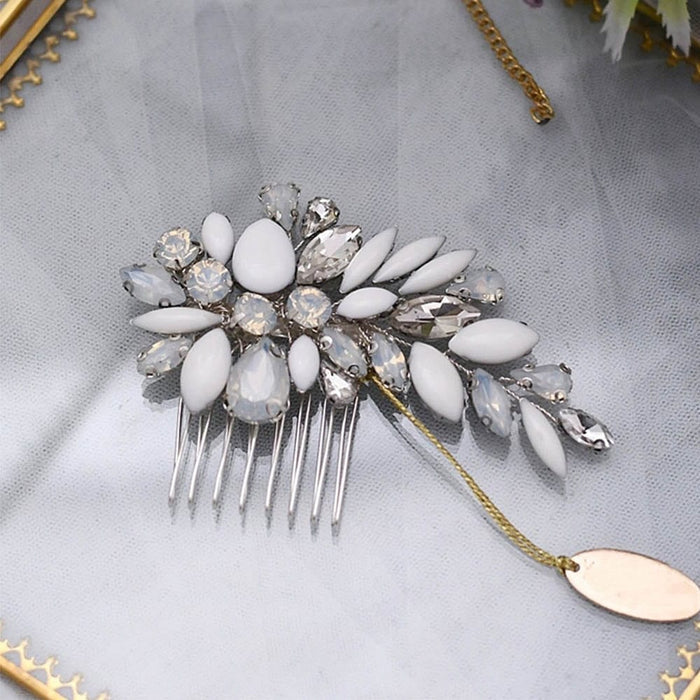 A decorative hair comb with silver prongs, white and clear floral-and-leaf gemstones, plus a gold chain and oval charm for elegance.