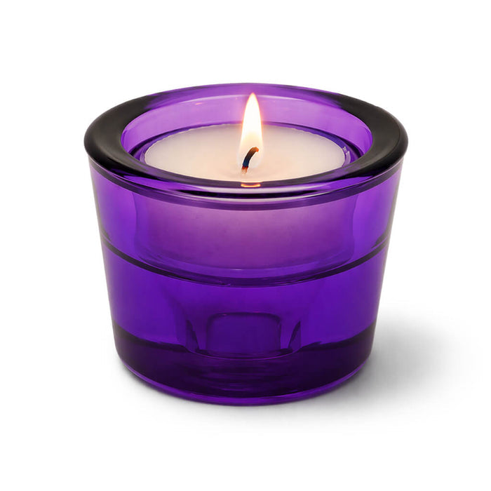 Lit tea light candle in a purple glass holder on a white background