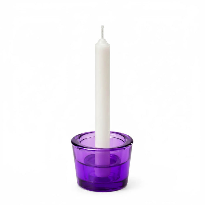 White taper candle in a purple glass holder on a white background
