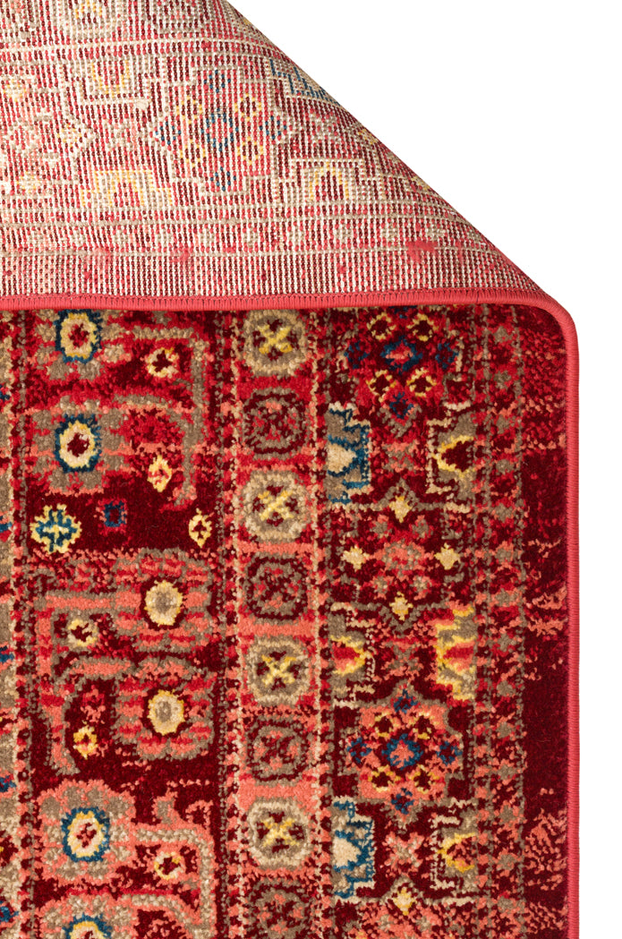 Deep red traditional rug with a geometric medallion pattern in blue, yellow, and beige, shown with a folded corner.