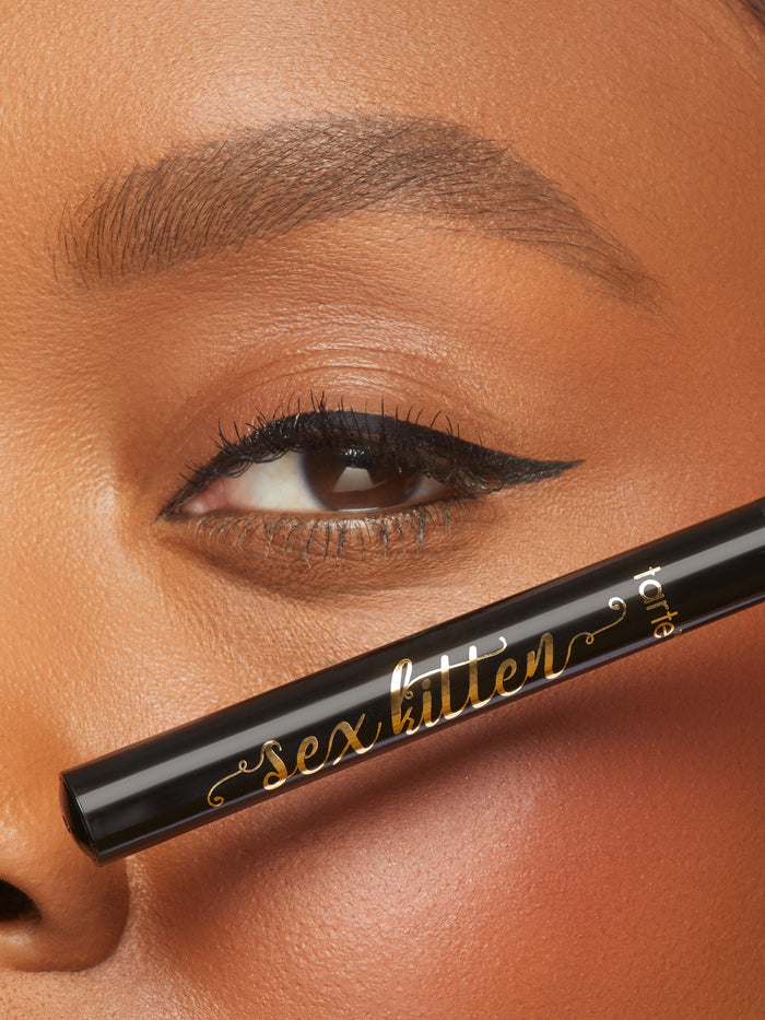 Eyeliner pencil labeled 'sex kitten' being used on a model's eyelid.