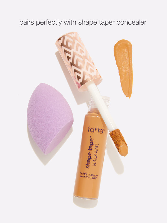 Tarte Shape Tape concealer with applicator and purple makeup sponge on a white background