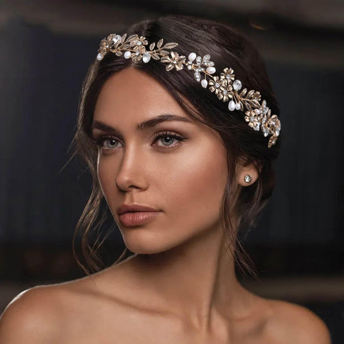 A woman with long brown hair in an updo wears a gold floral headpiece with pearls and crystals, gazing elegantly to the side.